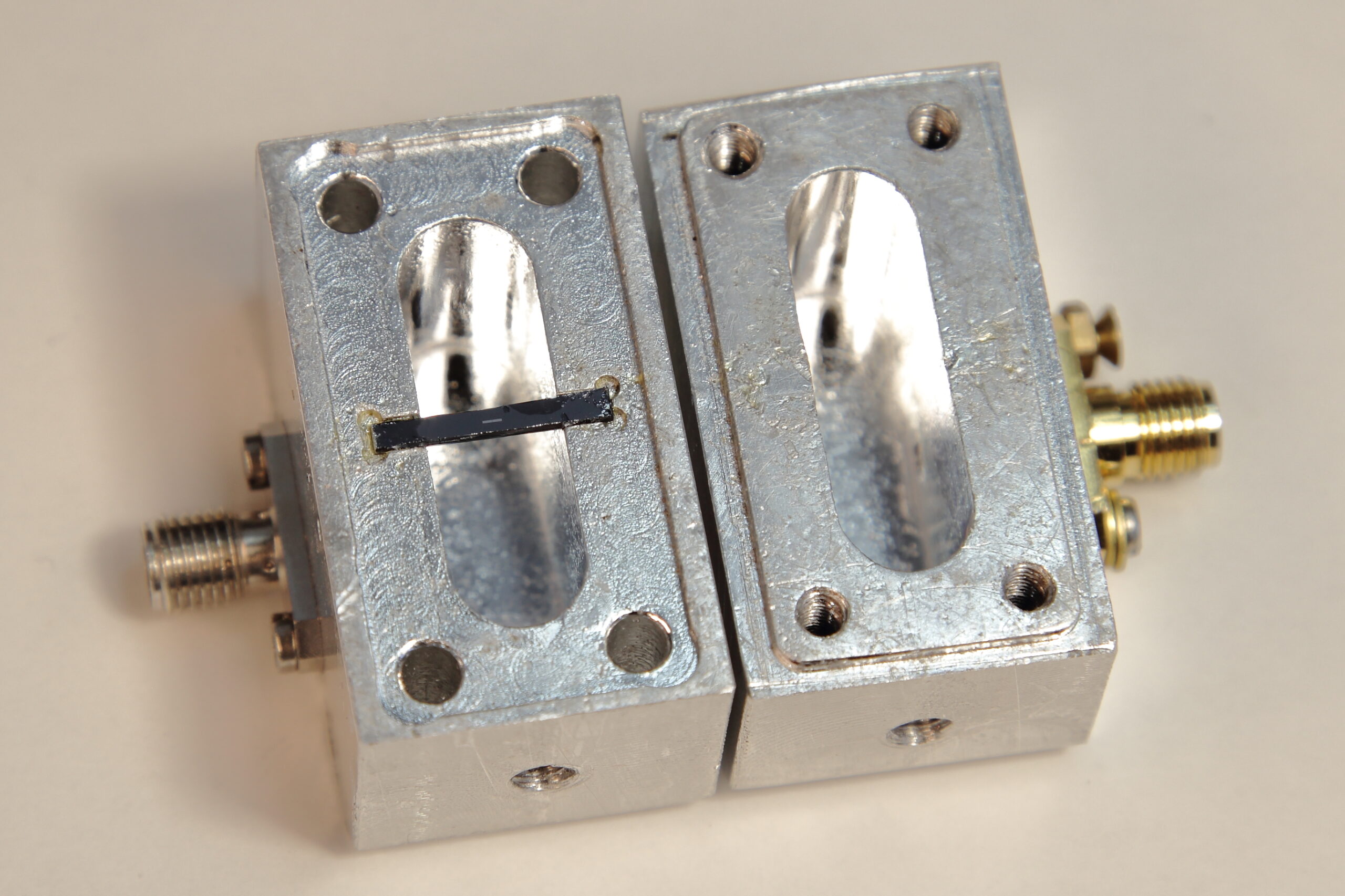La foto mostra la cavità superconduttiva risonante aperta. Nella parte sinistra, al centro, è visibile il supporto rettangolare nero sul quale è depositato il circuito del qubit, riconoscibile come una piccola linea grigia.